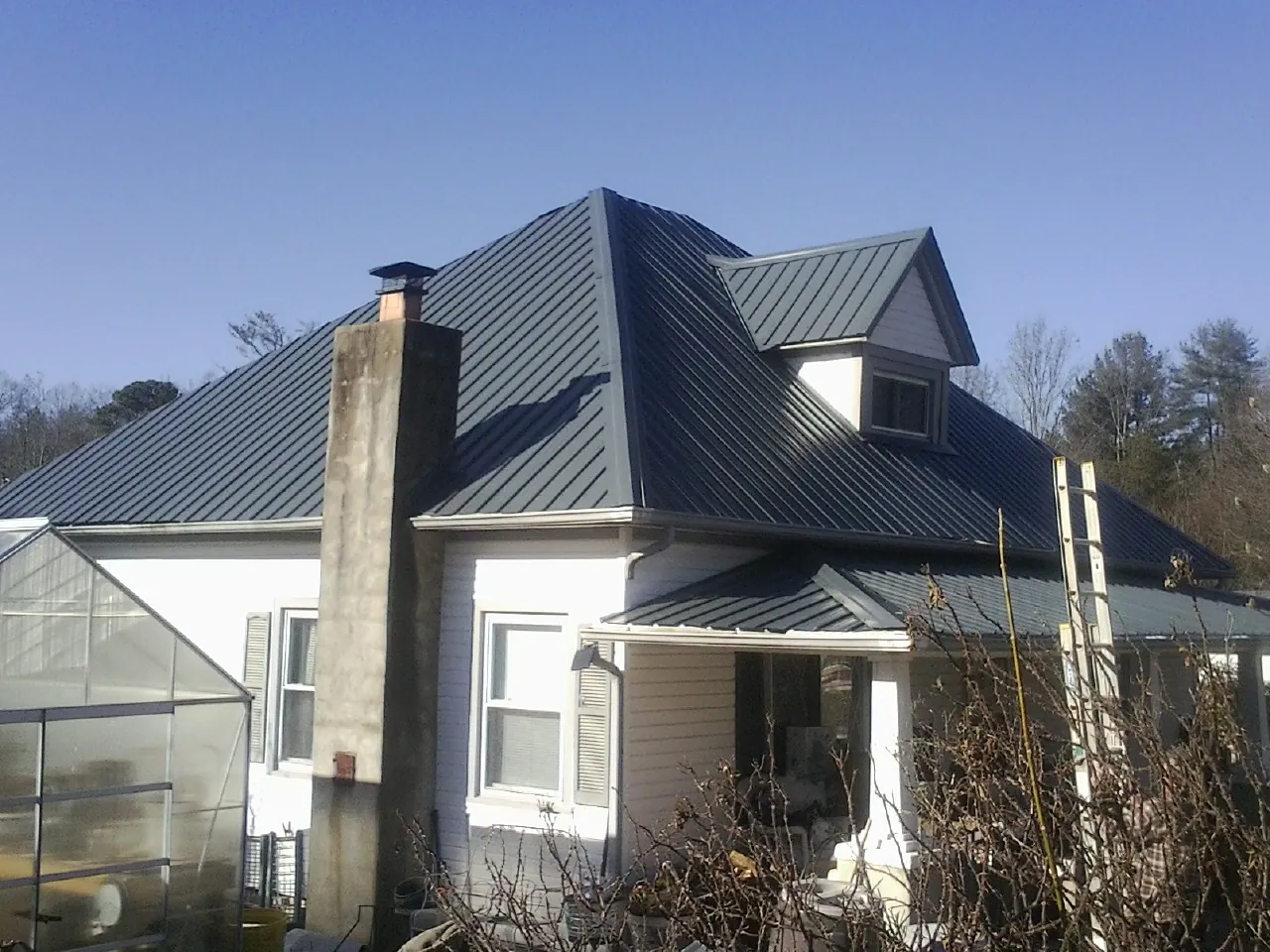 Dark blue standing seam metal roof on a white farmhouse with dormer — Slate & Tile Roof Repair by Roofing Brothers in Markleton