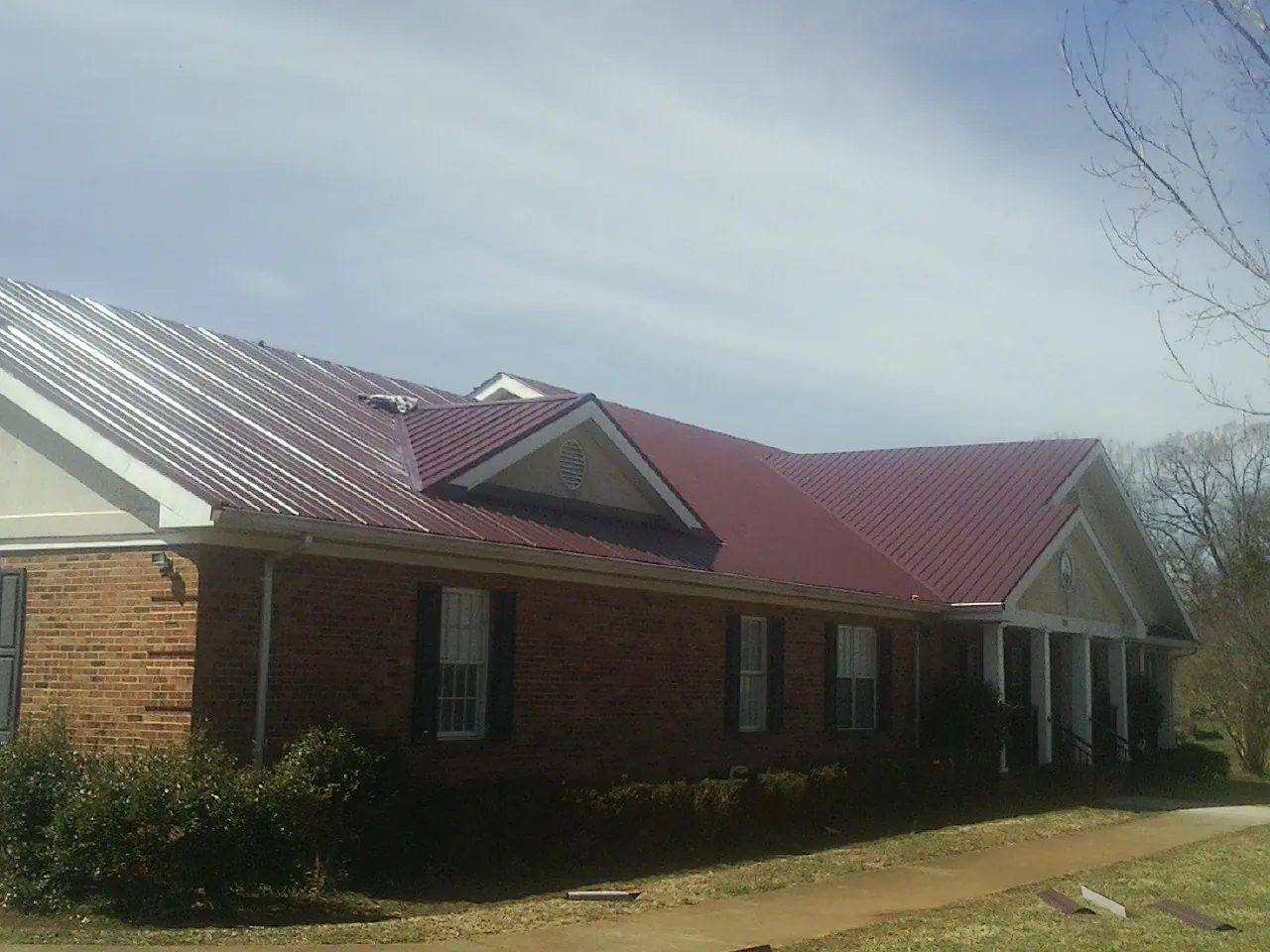 Red metal roof with gabled entries on a long brick building, from a Hail Damage Roof Repair job in Markleton