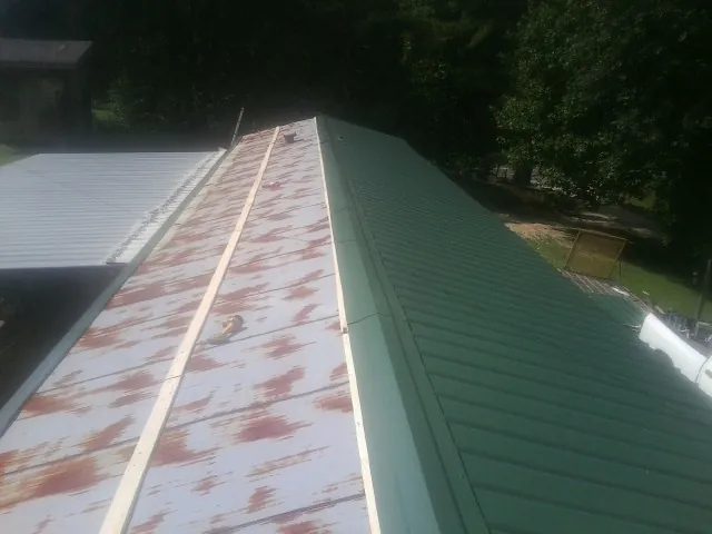 Old rusted panels beside newly installed green metal roofing — Wind Damage Roof Repair by Roofing Brothers in Markleton
