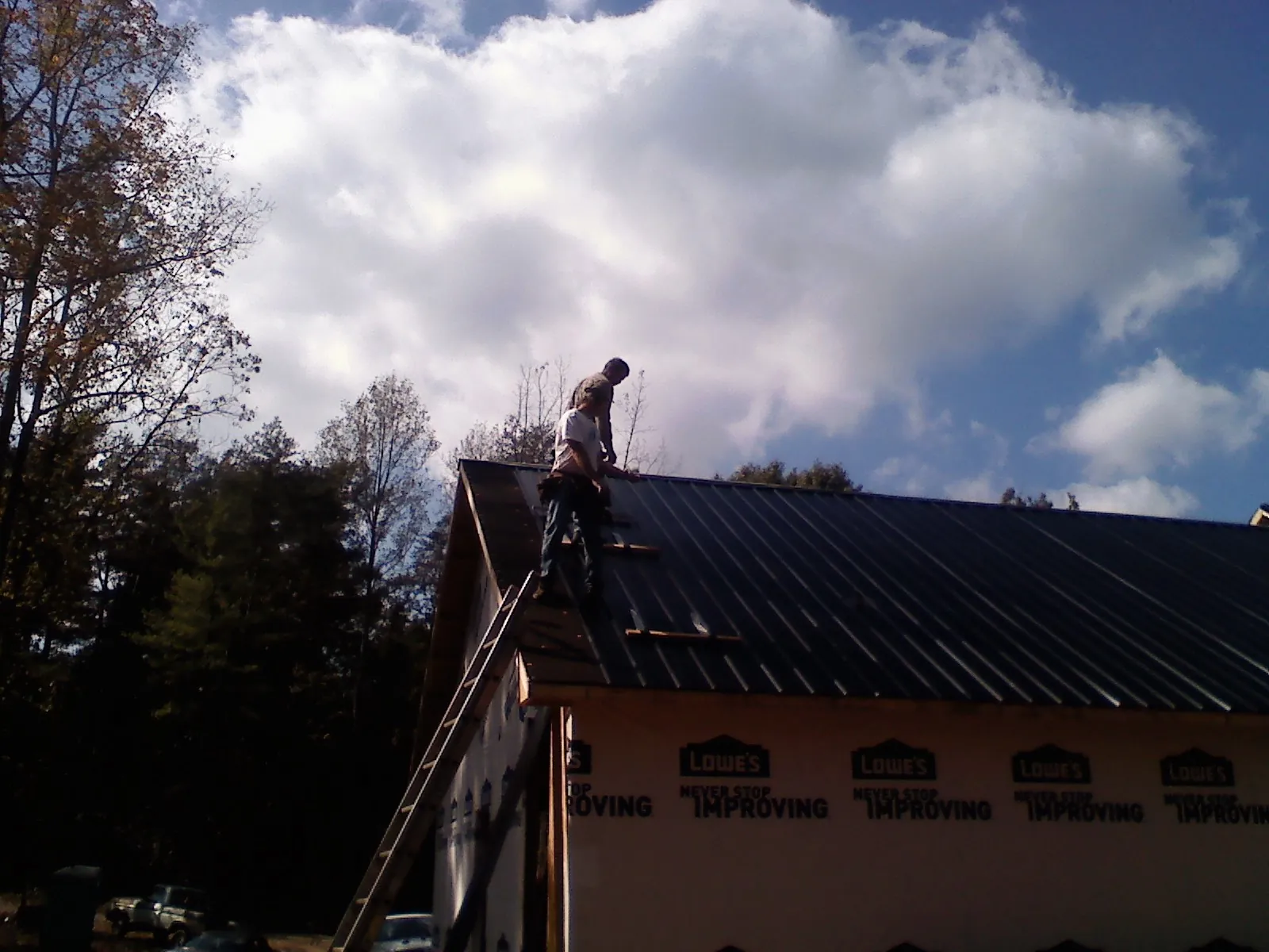 Roofer fastening dark metal panels high against a cloudy sky, from a Roof Inspection job in Markleton