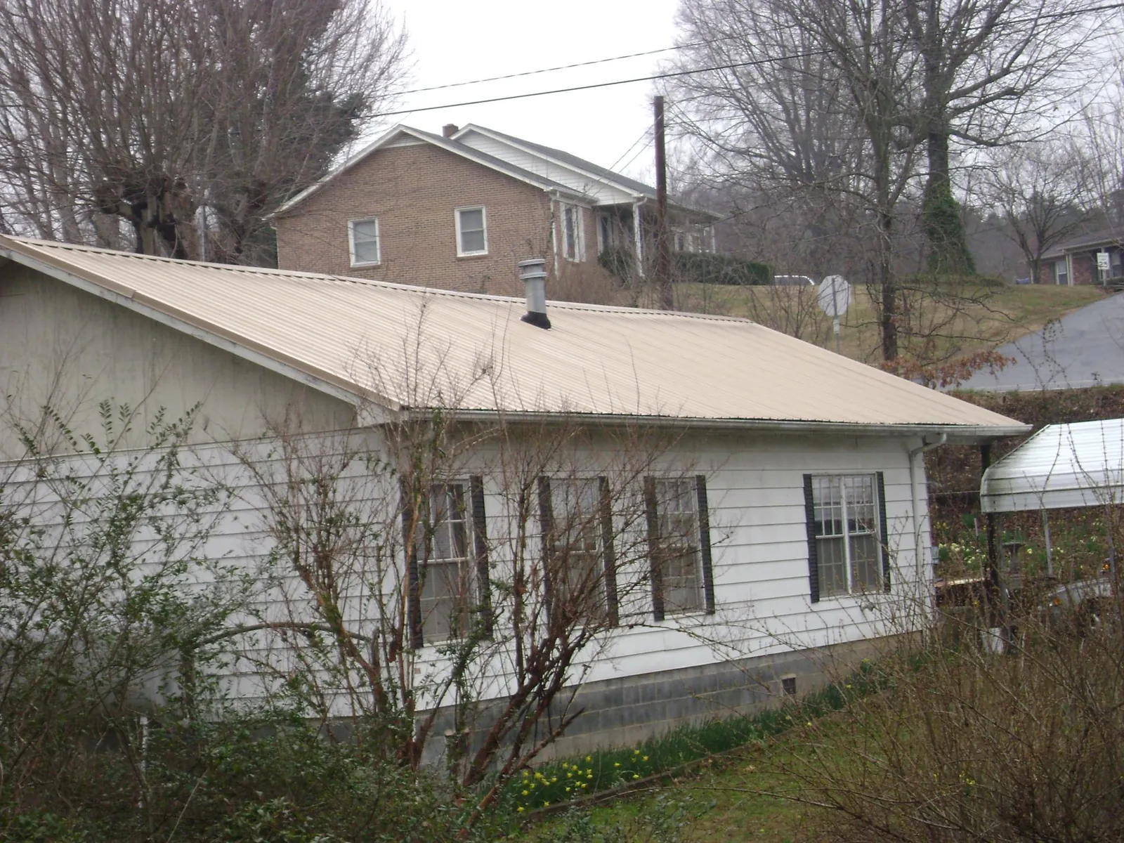 Tan metal roof on a white sided house set into a hillside — Commercial Roofing by Roofing Brothers in Markleton